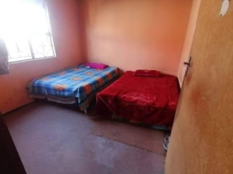 A basic bedroom featuring a window with security bars and plain wall finishes, requiring cosmetic updates to improve its overall condition.