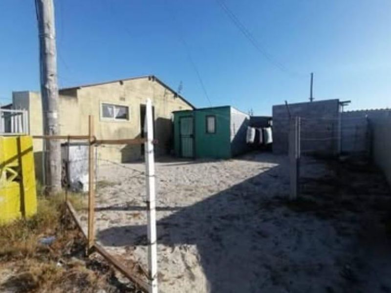 Rear exterior view of the property featuring a sandy yard, basic boundary fencing, and a small detached utility structure.