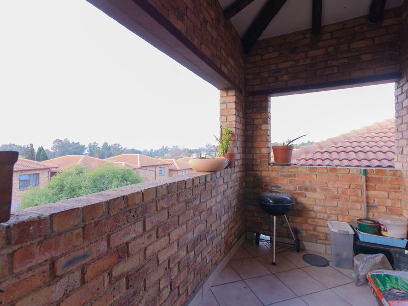 A covered balcony featuring exposed brick walls, tiled flooring, and timber rafters, offering an open view of the surrounding residential area.