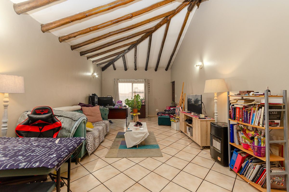 Spacious living room featuring a high vaulted ceiling with exposed timber rafters and neutral ceramic floor tiles, leading to a sliding glass door.
