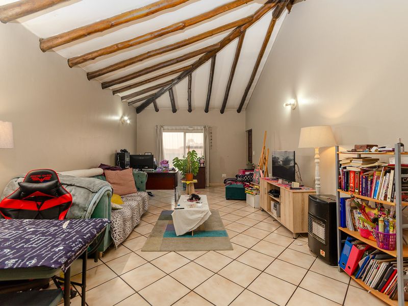 Spacious living room featuring a high vaulted ceiling with exposed timber rafters and neutral ceramic floor tiles, leading to a sliding glass door.