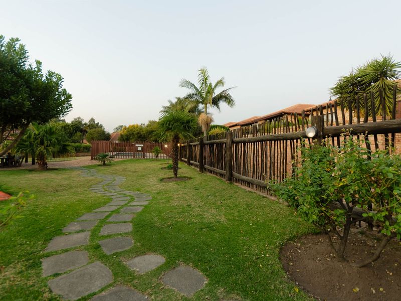 A well-maintained communal garden area featuring a winding stone pathway, established landscaping, and rustic timber pole fencing.