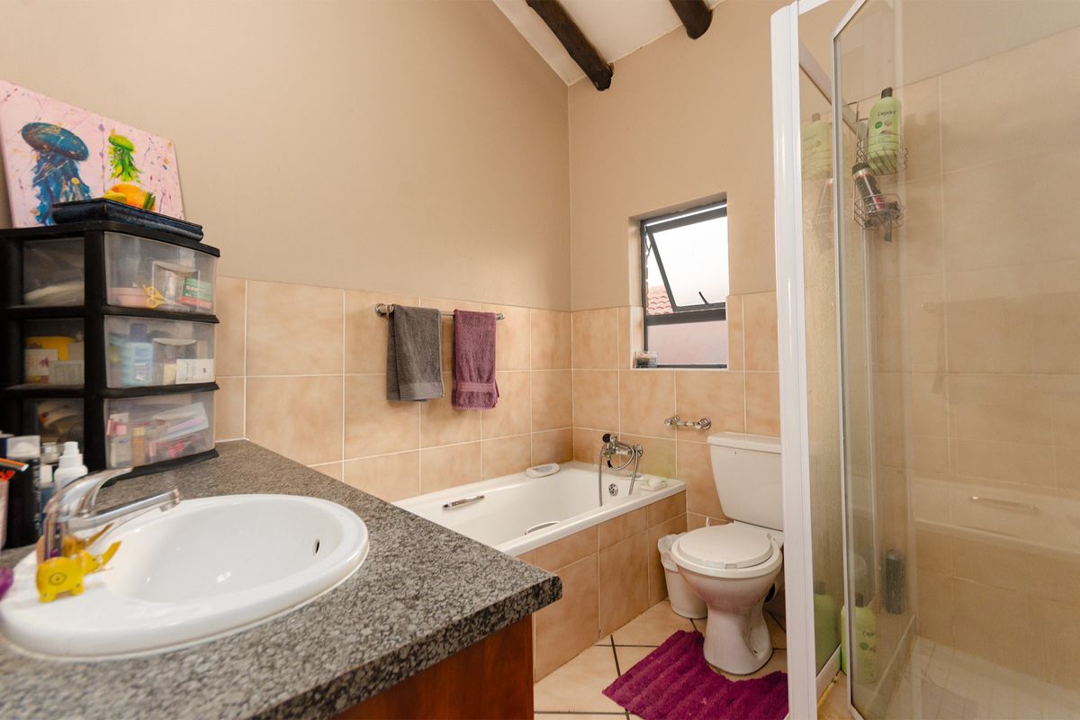 A functional bathroom featuring a granite-topped vanity, a bathtub, a separate shower enclosure, and tiled finishes with exposed ceiling beams.