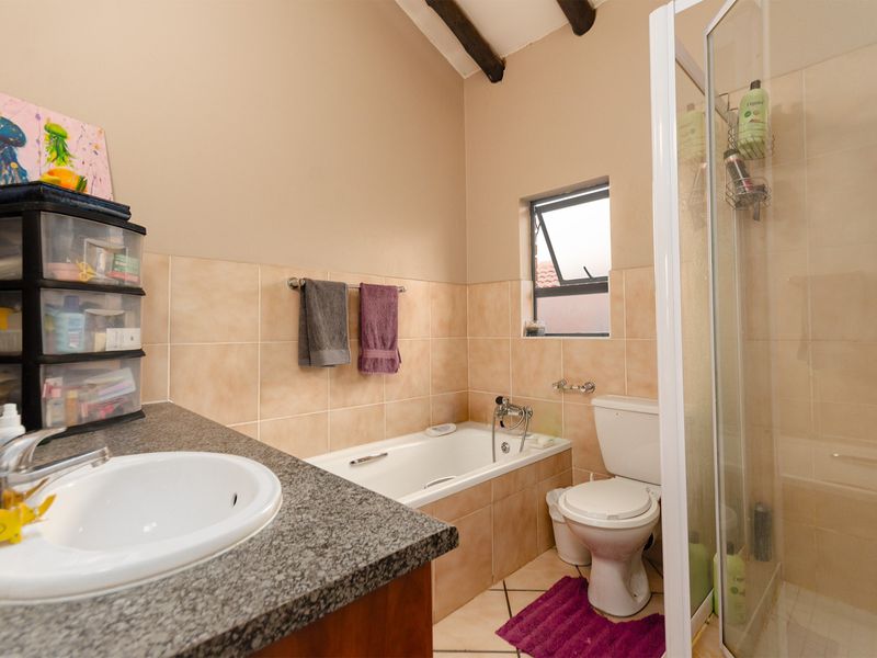 A functional bathroom featuring a granite-topped vanity, a bathtub, a separate shower enclosure, and tiled finishes with exposed ceiling beams.