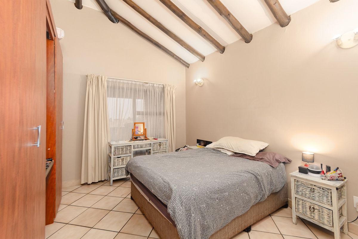 A bedroom featuring exposed timber ceiling beams, tiled flooring, and a built-in wardrobe, offering a rustic aesthetic with neutral wall tones.