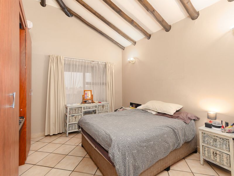 A bedroom featuring exposed timber ceiling beams, tiled flooring, and a built-in wardrobe, offering a rustic aesthetic with neutral wall tones.