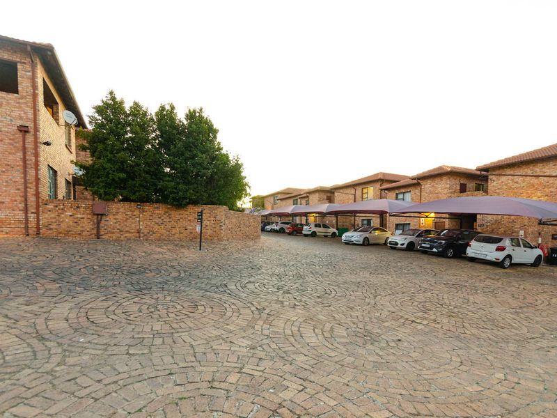 Exterior view of an apartment complex featuring brick facade buildings, paved driveway, and covered parking bays.
