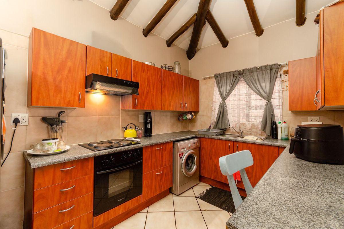A functional kitchen featuring warm-toned wooden cabinetry, granite countertops, built-in appliances, and distinctive exposed wooden ceiling beams.