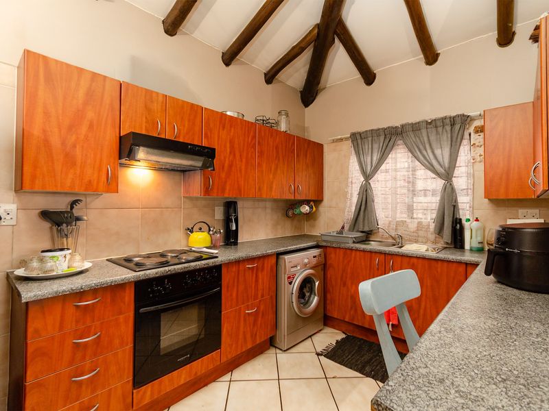 A functional kitchen featuring warm-toned wooden cabinetry, granite countertops, built-in appliances, and distinctive exposed wooden ceiling beams.