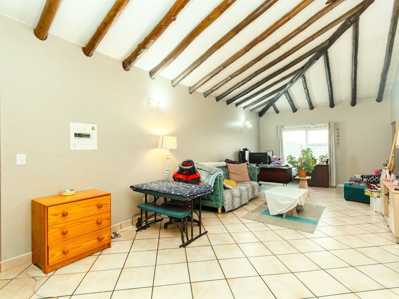 Spacious living area featuring a vaulted ceiling with exposed timber beams and neutral ceramic floor tiles.
