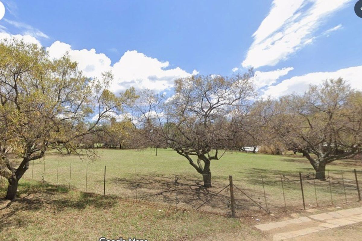 A spacious, open garden area featuring mature trees and perimeter wire fencing, offering a natural and expansive outdoor setting.