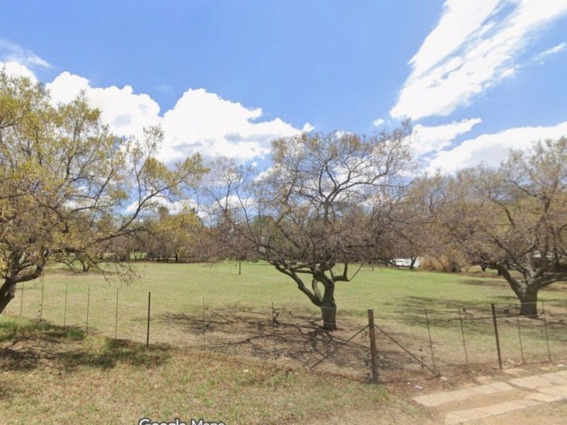 A spacious, open garden area featuring mature trees and perimeter wire fencing, offering a natural and expansive outdoor setting.