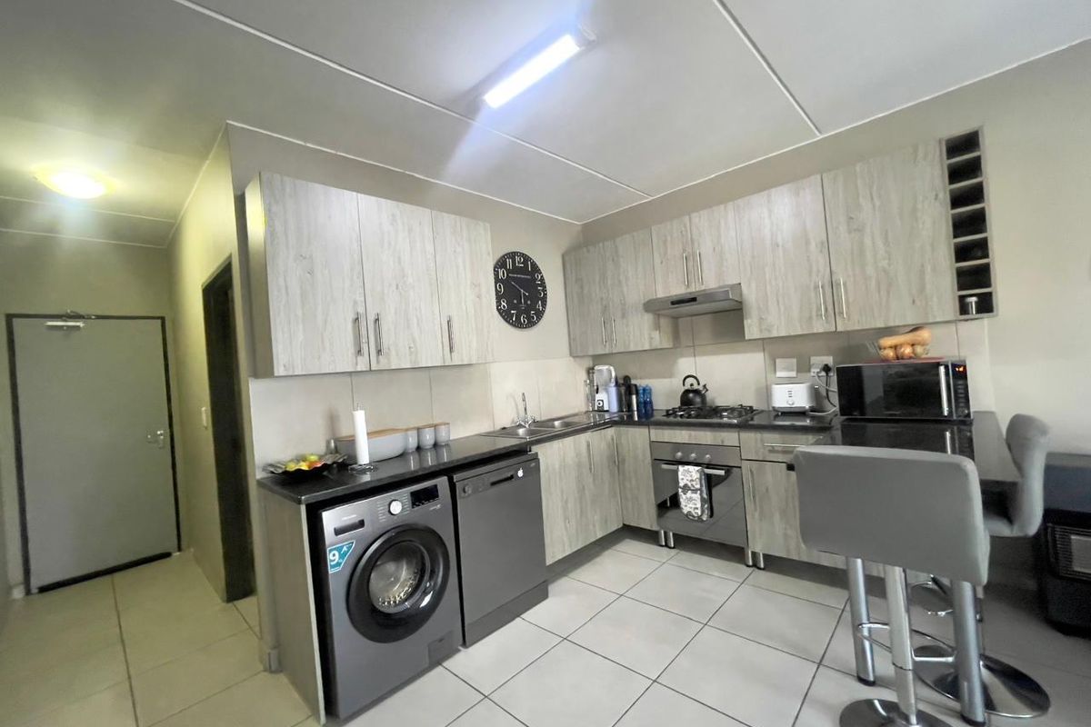 Modern kitchen featuring light wood-grain cabinetry, dark countertops, tiled flooring, and integrated appliances including an oven, hob, and extractor fan.
