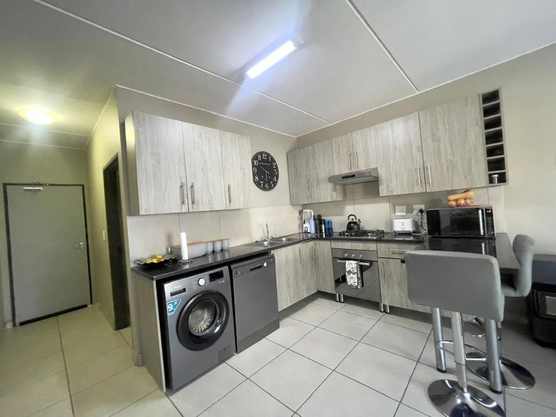 Modern kitchen featuring light wood-grain cabinetry, dark countertops, tiled flooring, and integrated appliances including an oven, hob, and extractor fan.