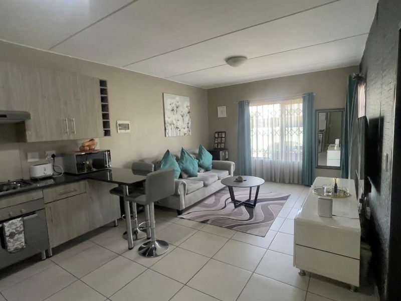 An open-plan living area featuring a compact kitchen with built-in cabinetry, hob, and oven, seamlessly flowing into a comfortable lounge space with tiled flooring.