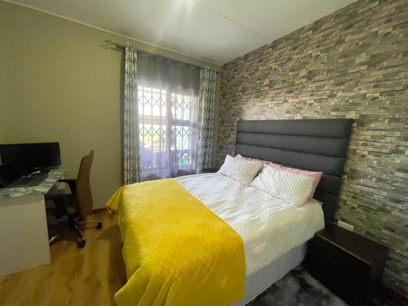 A bedroom featuring laminate flooring and a stone veneer accent wall, providing a textured focal point for the space.