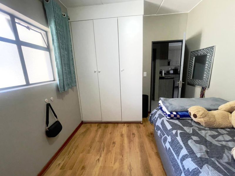 A functional bedroom featuring laminate flooring, a built-in wardrobe, and natural light from a side window.