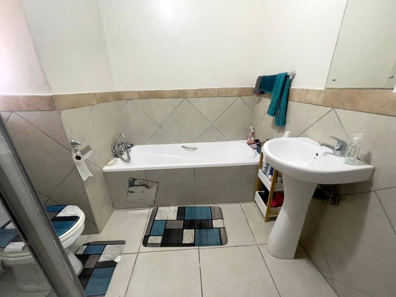 A functional bathroom featuring a bathtub with a tiled apron, a pedestal basin, and neutral wall and floor tiling.