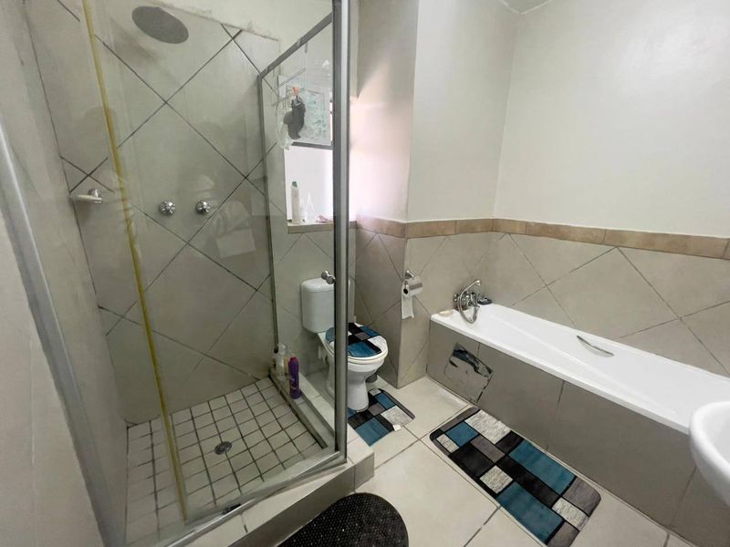 A functional bathroom featuring a separate shower enclosure, bathtub, and toilet with neutral wall and floor tiling.