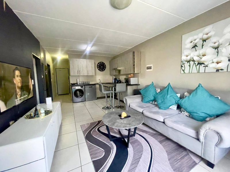 Open-plan living area featuring a compact kitchen with built-in cabinetry, tiled flooring, and integrated laundry facilities, creating a functional and versatile living space.
