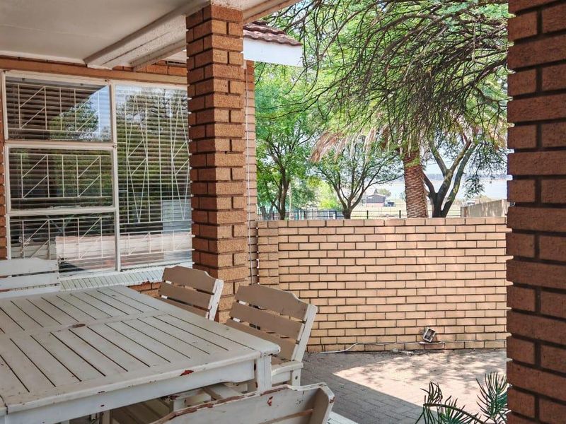 Covered patio area featuring brick pillars and tiled flooring, overlooking a private garden space with mature trees.