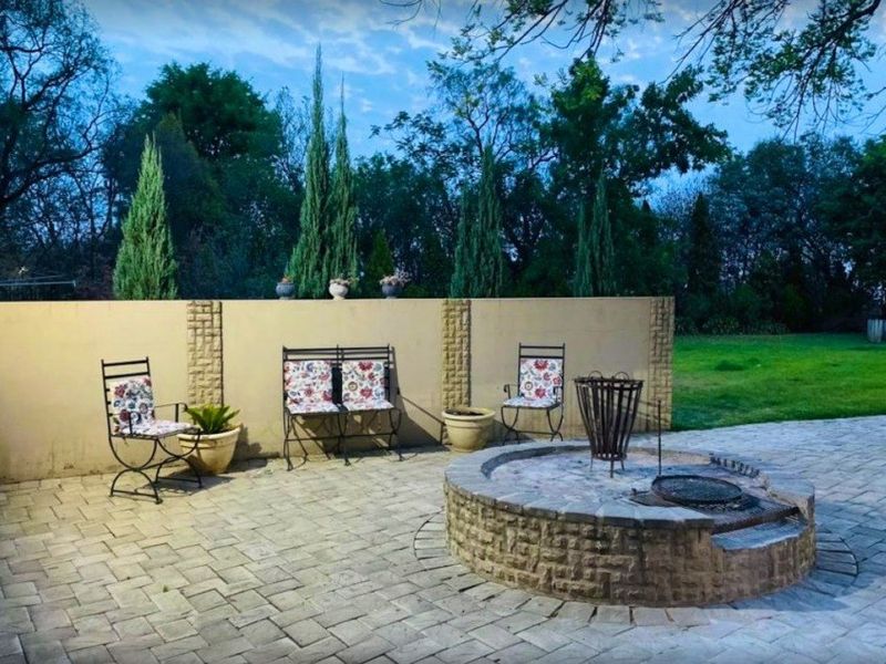 An outdoor paved patio area featuring a built-in stone fire pit and a solid boundary wall, set within a landscaped garden environment.