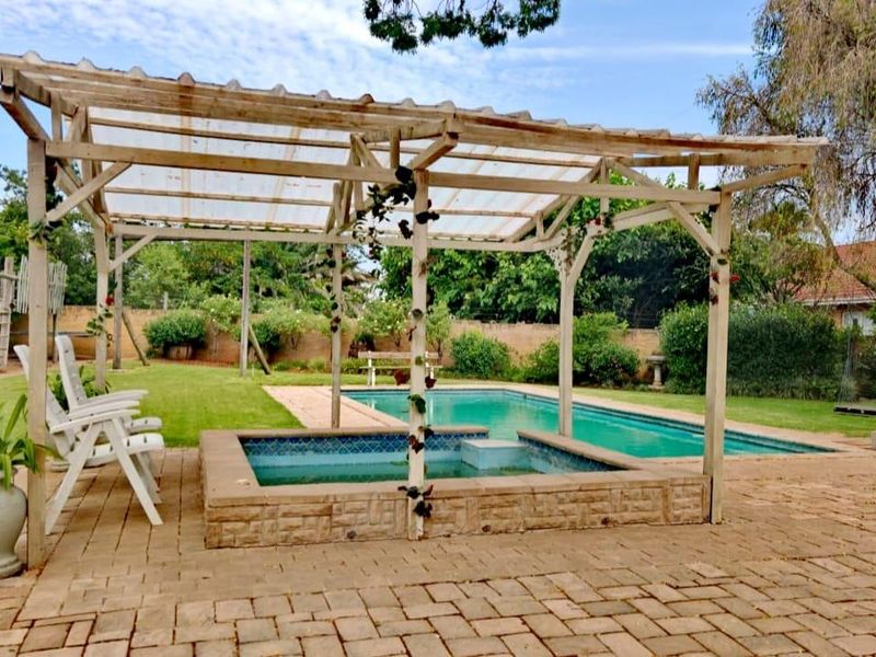 Outdoor pool area featuring a swimming pool, raised spa, and a timber pergola set on brick paving within a landscaped garden.
