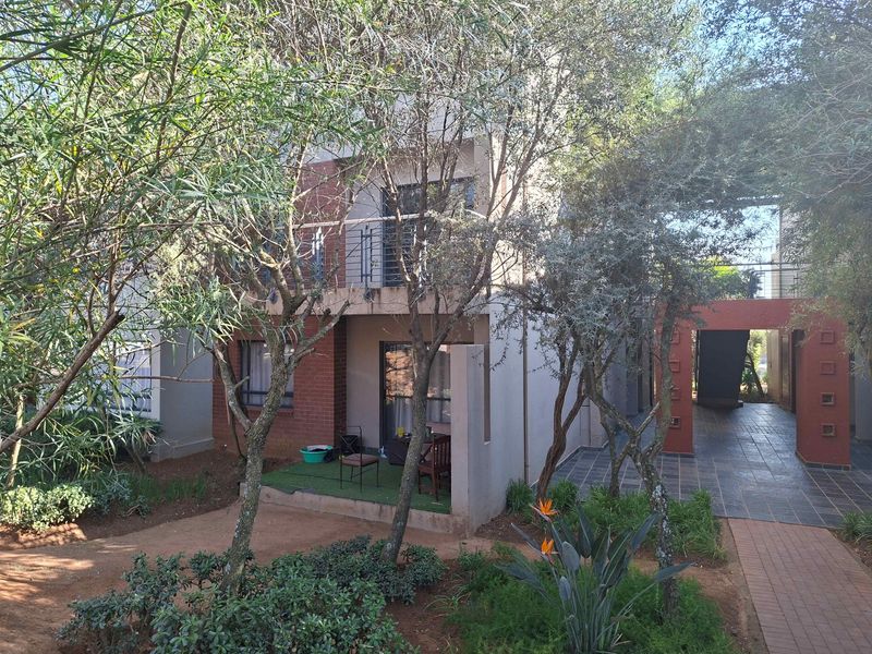 Rear view of a multi-story apartment building featuring a ground-floor patio, upper-level balcony, brick accents, and a landscaped garden area.