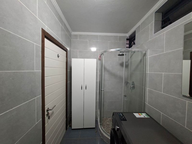 A modern bathroom featuring grey wall tiles, a curved glass shower enclosure, and a high-level ventilation window.