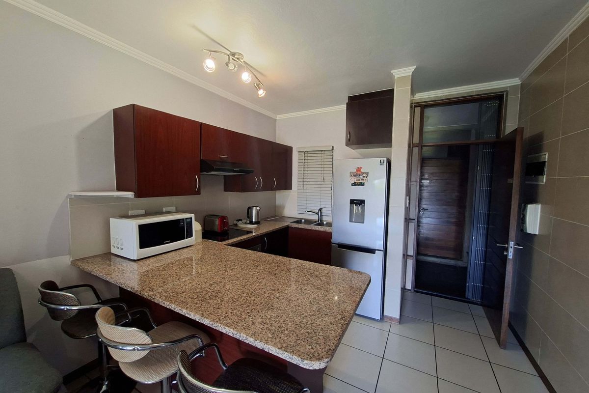 Compact kitchen featuring granite countertops, built-in cabinetry, a breakfast bar, and tiled flooring, providing a functional space for cooking and dining.