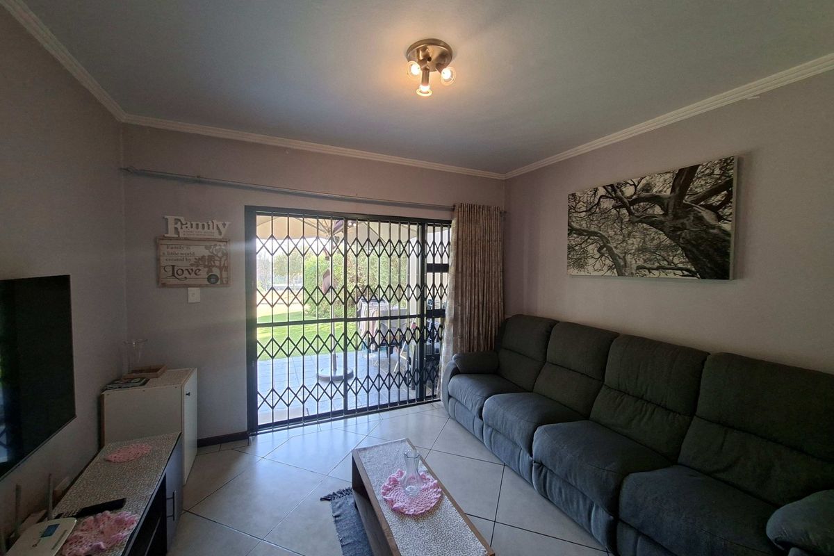 A living room featuring tiled flooring, a ceiling light fixture, and a sliding glass door with a security gate leading to the outdoor area.