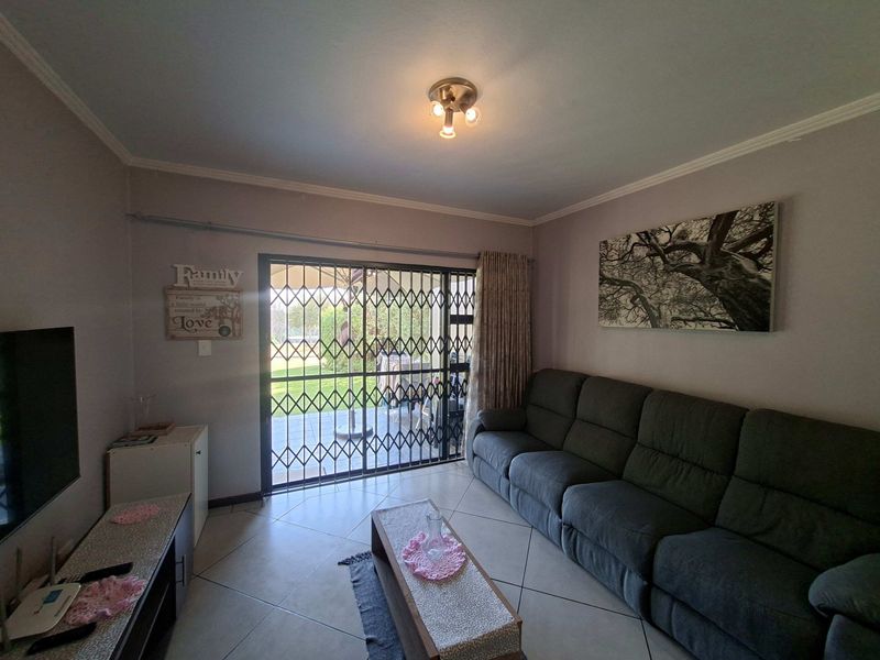 A living room featuring tiled flooring, a ceiling light fixture, and a sliding glass door with a security gate leading to the outdoor area.