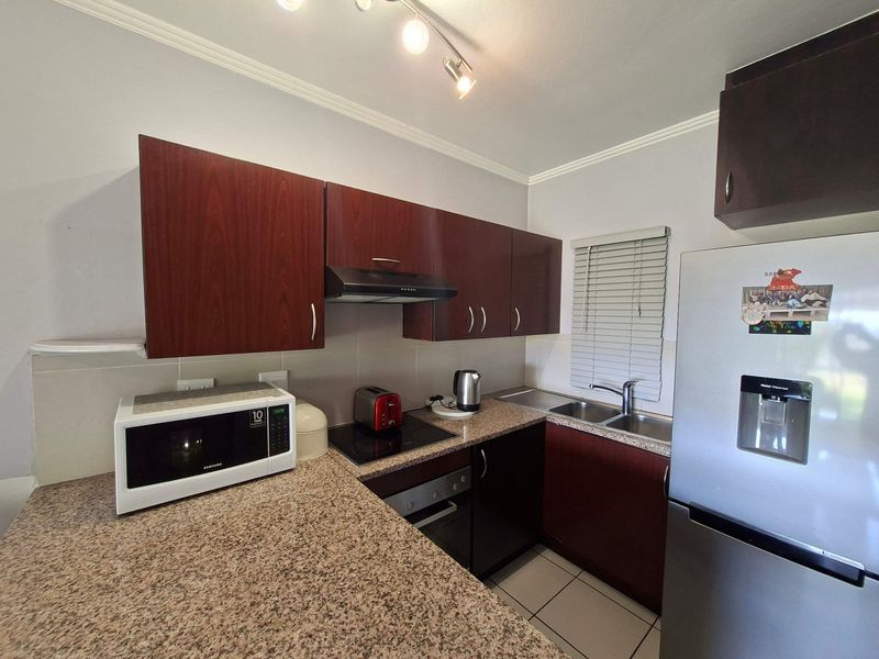 Compact kitchen featuring dark wood-finish cabinetry, granite countertops, built-in oven, electric hob, and a stainless steel double sink with tiled flooring.