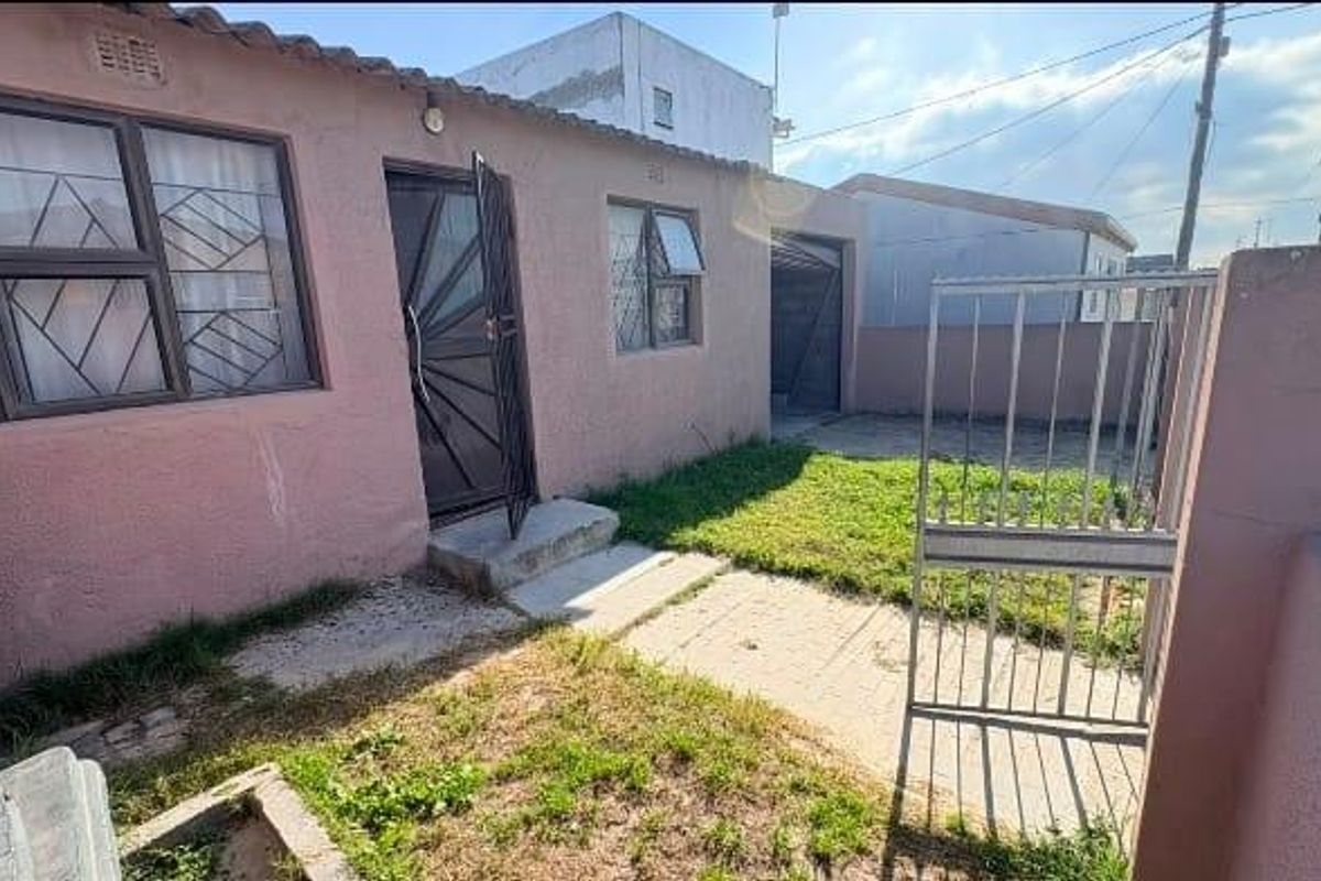 Rear exterior view of the property featuring a paved walkway, security gates, and a small garden area with boundary walls.