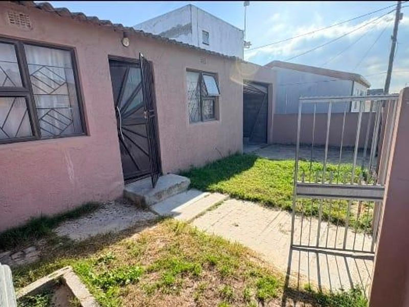 Rear exterior view of the property featuring a paved walkway, security gates, and a small garden area with boundary walls.