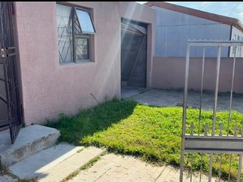 Front exterior view of the property featuring a paved driveway, small lawn area, security gate, and metal security door entrance.