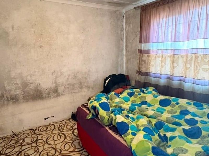 A bedroom requiring significant renovation, featuring worn flooring and walls with extensive staining and ceiling damage.