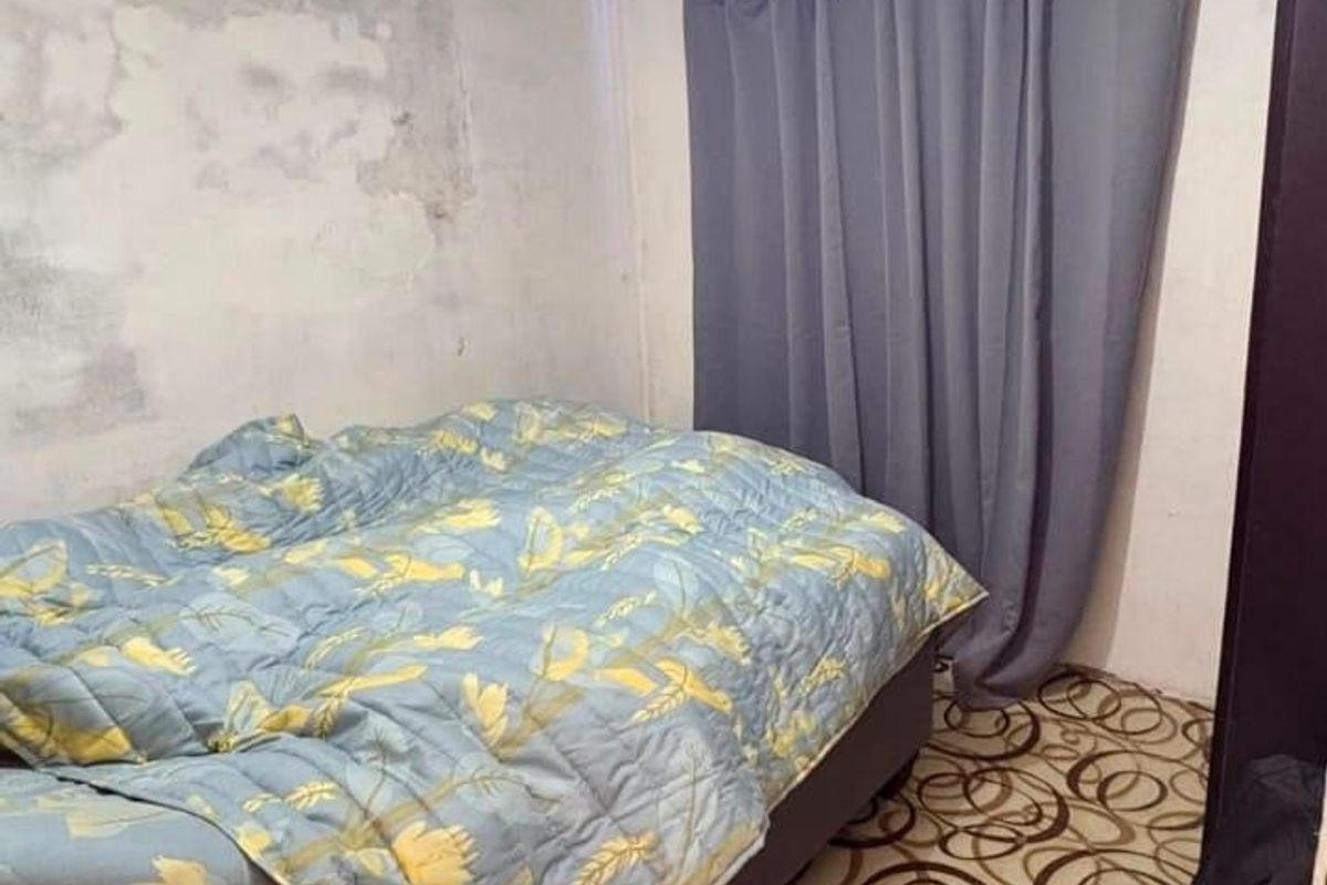 A bedroom featuring patterned flooring and visible signs of wall and ceiling deterioration requiring maintenance and cosmetic updates.