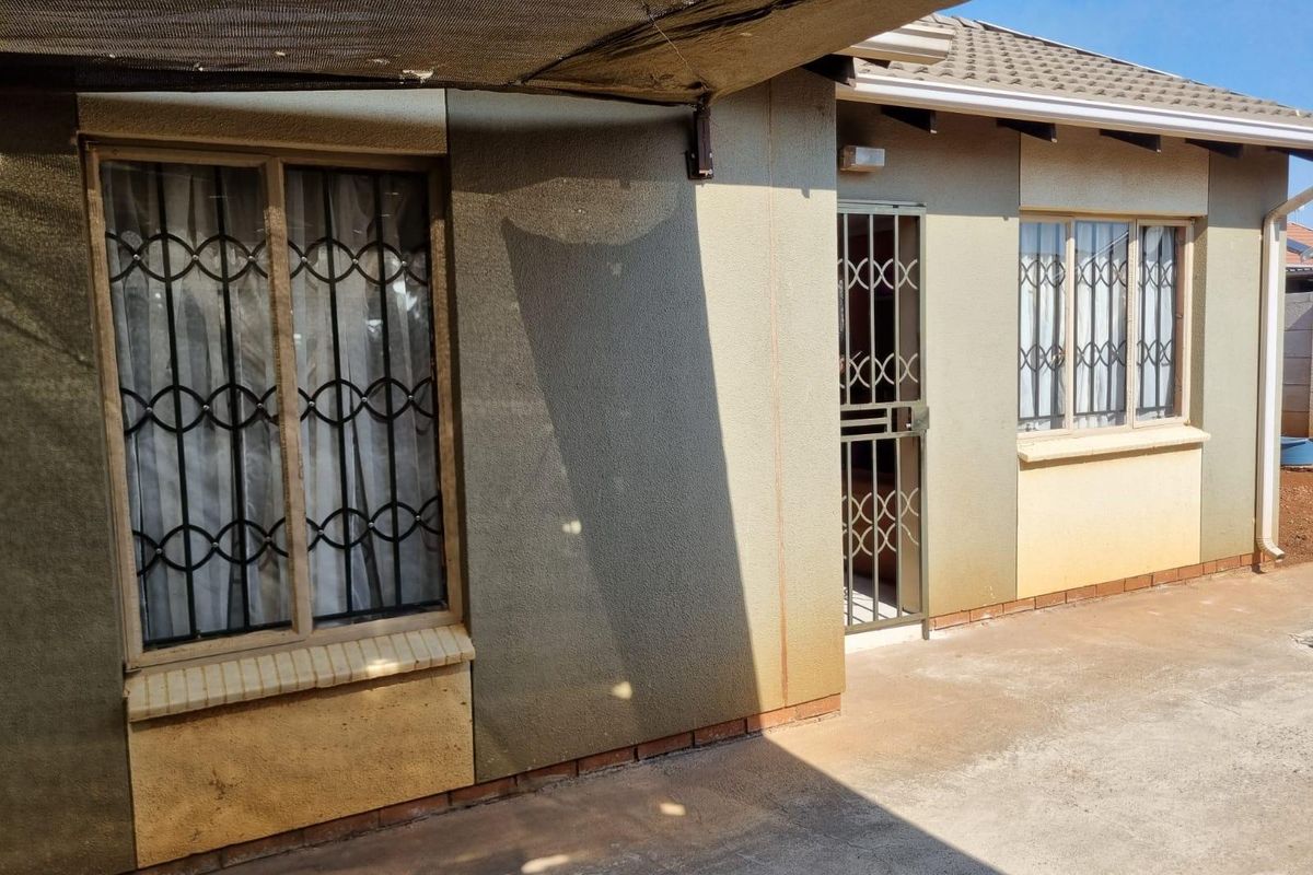 Rear exterior view of the property featuring a concrete patio area, shade cloth awning, and security gates on windows and doors.