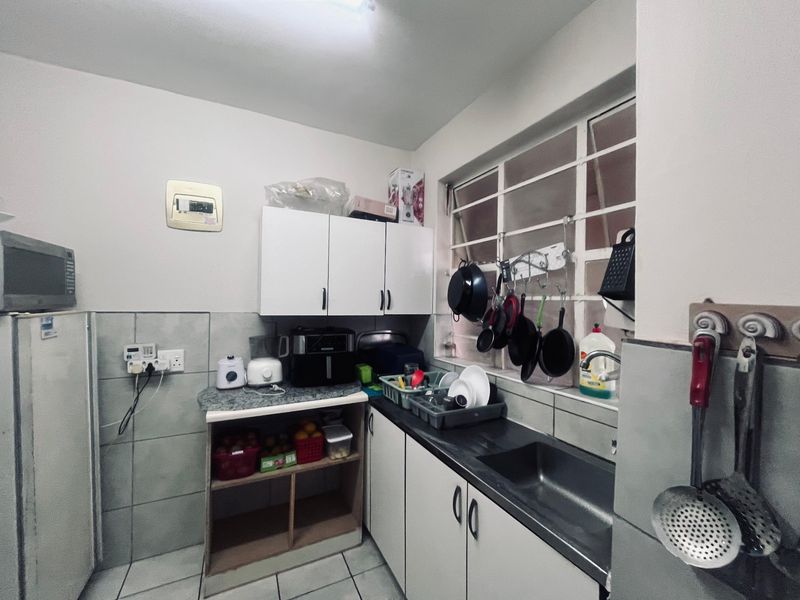 Compact kitchen featuring tiled finishes, built-in cabinetry, and a stainless steel sink, offering a functional layout with potential for cosmetic updates.