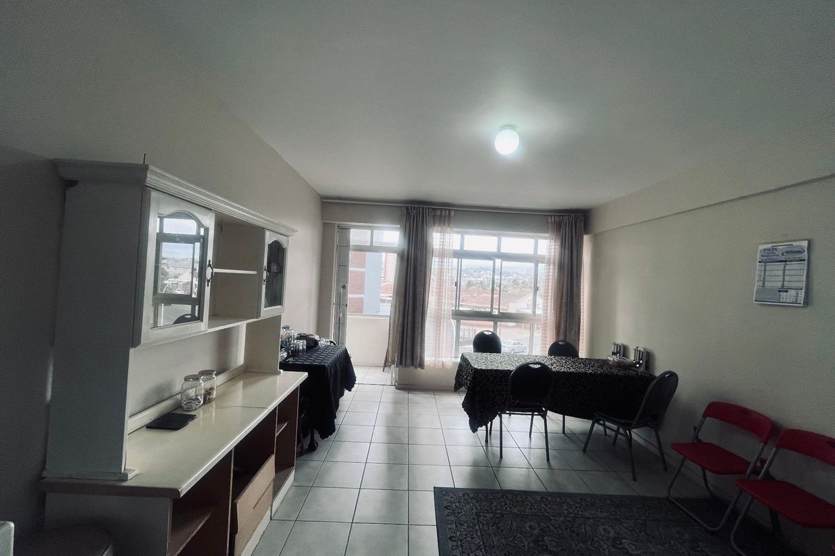 Spacious living area featuring neutral tiled flooring, large windows providing natural light, and direct access to an attached balcony.