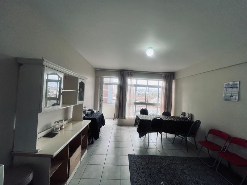 Spacious living area featuring neutral tiled flooring, large windows providing natural light, and direct access to an attached balcony.