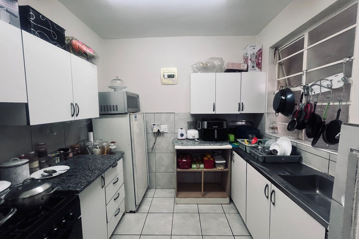 A functional kitchen featuring white cabinetry, granite countertops, tiled flooring, and a stainless steel sink, offering a practical layout for daily meal preparation.