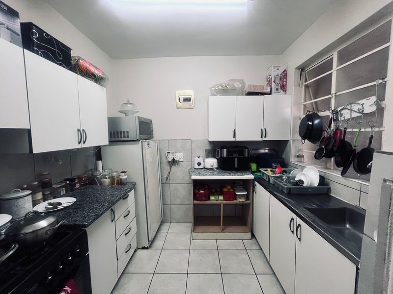 A functional kitchen featuring white cabinetry, granite countertops, tiled flooring, and a stainless steel sink, offering a practical layout for daily meal preparation.
