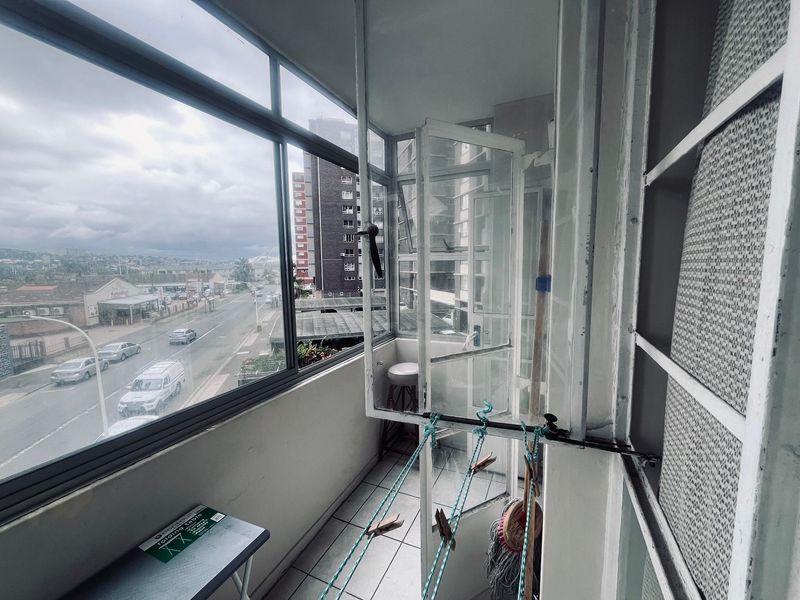 An enclosed balcony featuring tiled flooring and large windows with views of the surrounding street and urban landscape.