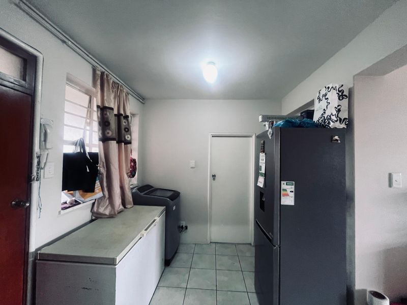 A functional laundry area featuring tiled flooring, a window with security bars, and an internal door providing access to the rest of the apartment.