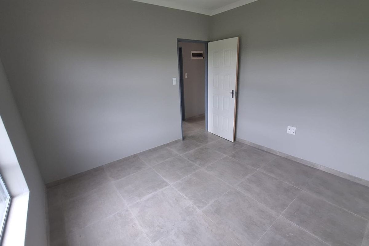 A clean, empty bedroom featuring neutral grey walls, modern large-format floor tiles, and a white internal door.