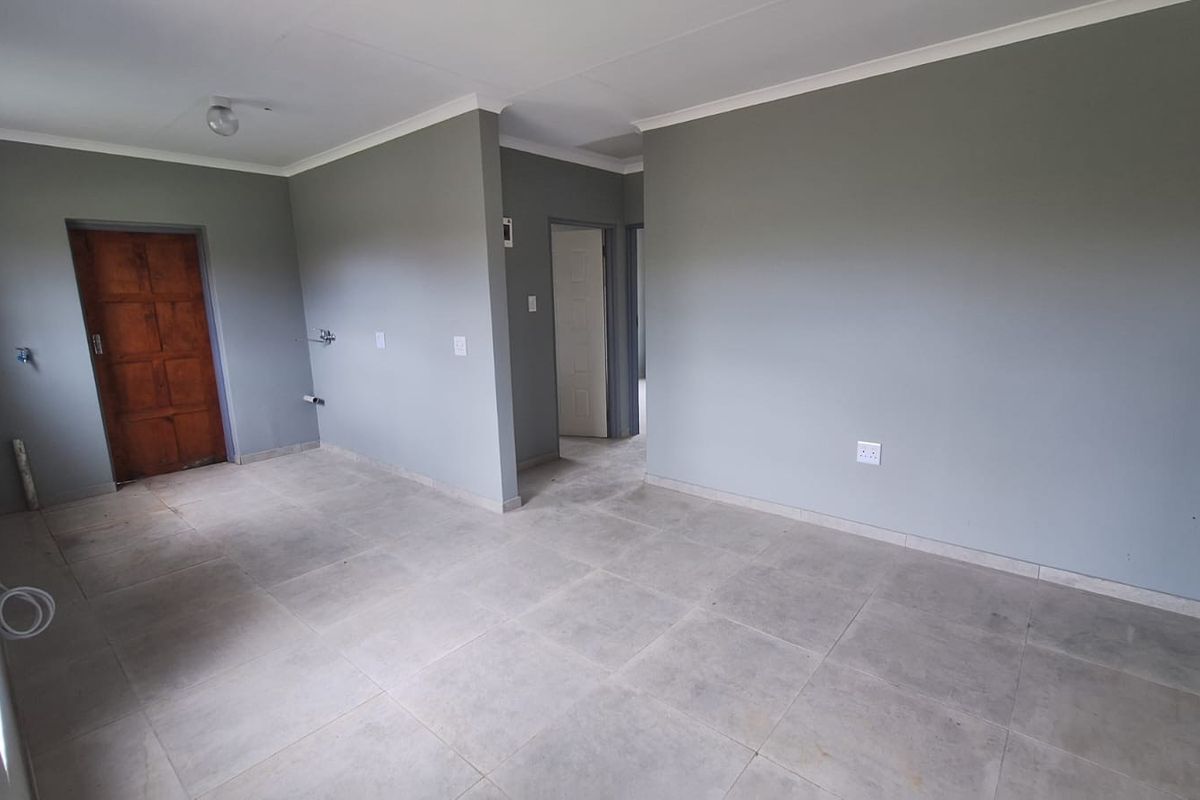 An empty, open-plan living area featuring neutral grey walls, tiled flooring, and coved ceilings, providing a blank canvas for interior design.