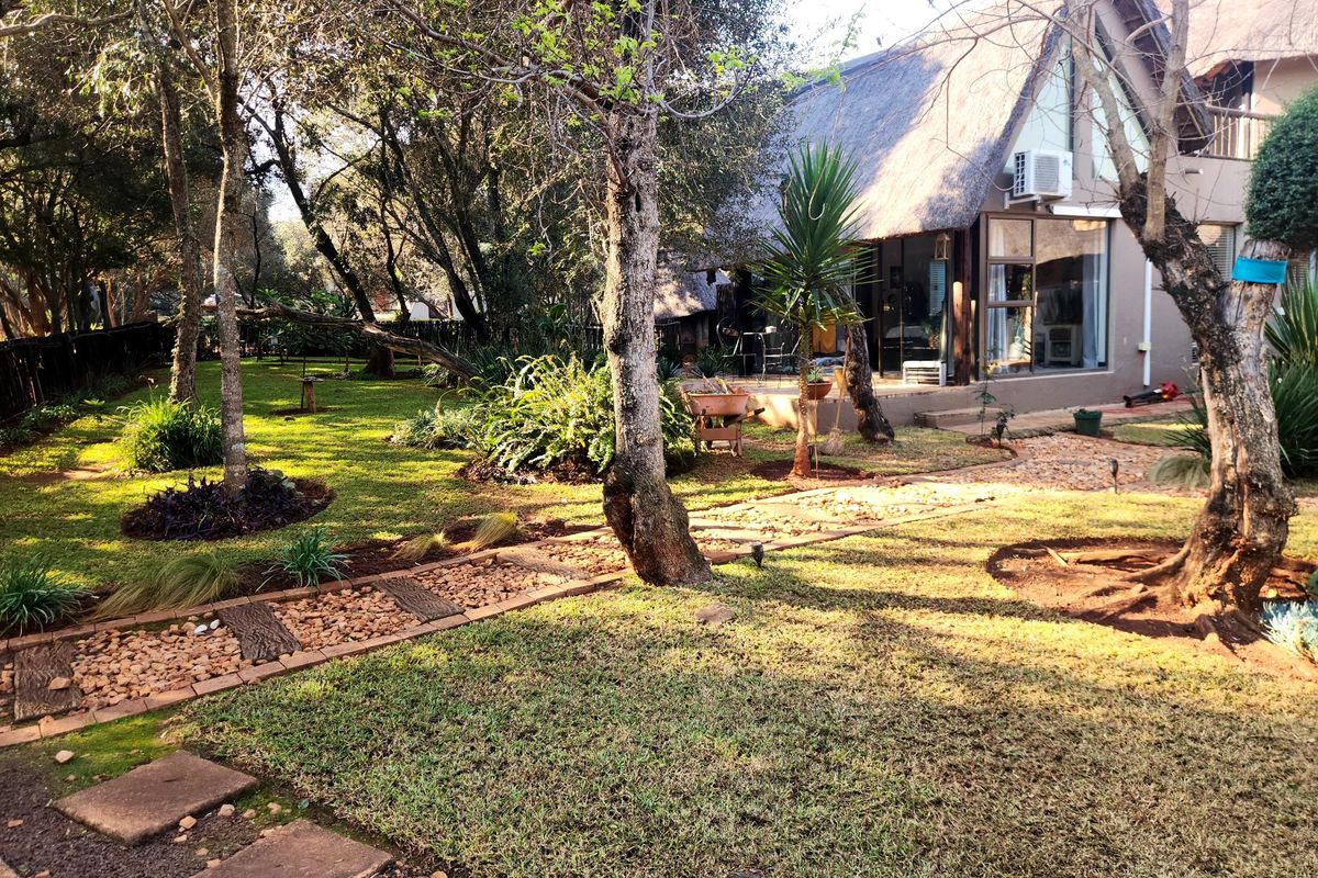 A view of the rear garden featuring a landscaped lawn, stone-paved pathways, and the rear facade of a house with a traditional thatched roof.