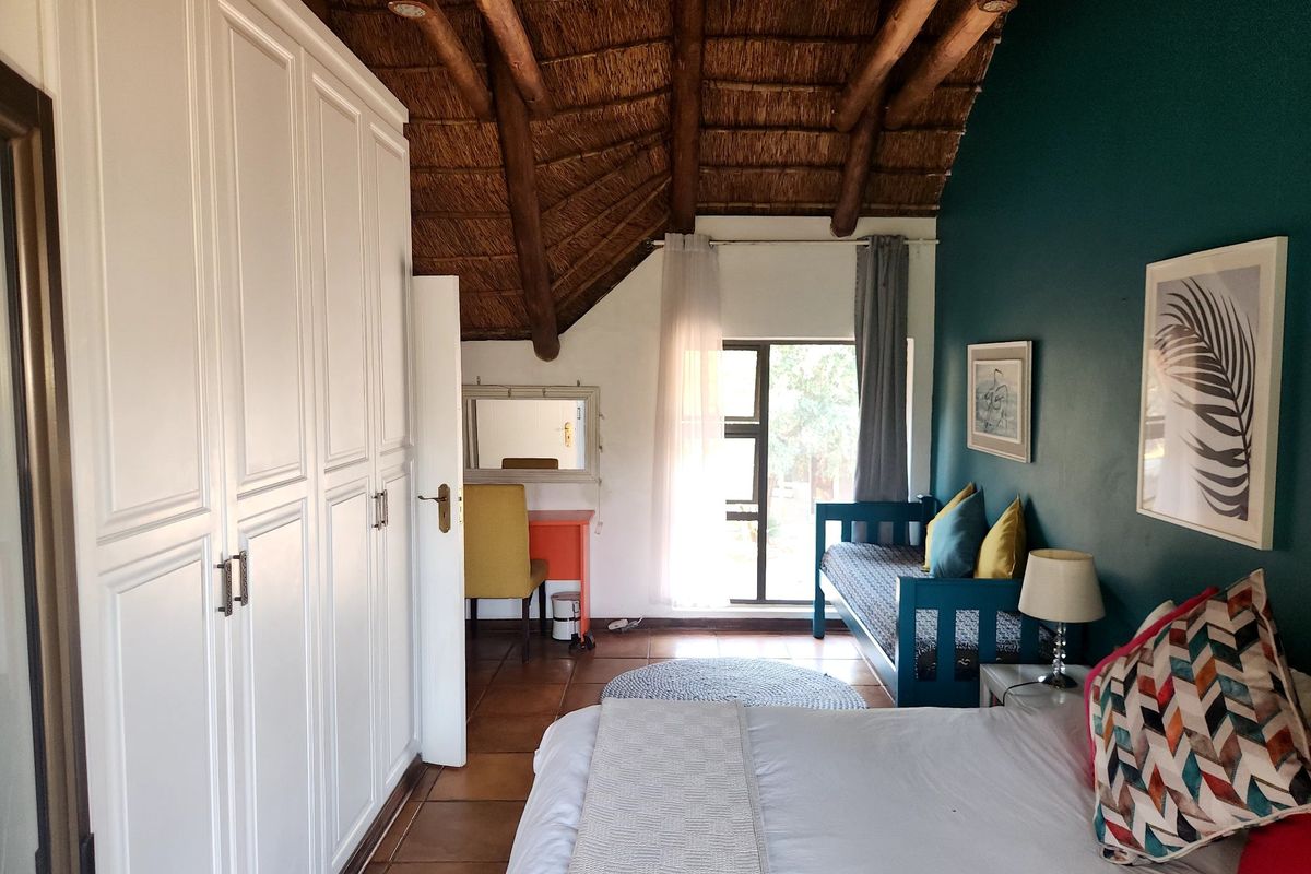 A cozy bedroom featuring a unique thatched roof with exposed timber rafters, built-in cupboards, and tiled flooring, offering a warm and rustic atmosphere.
